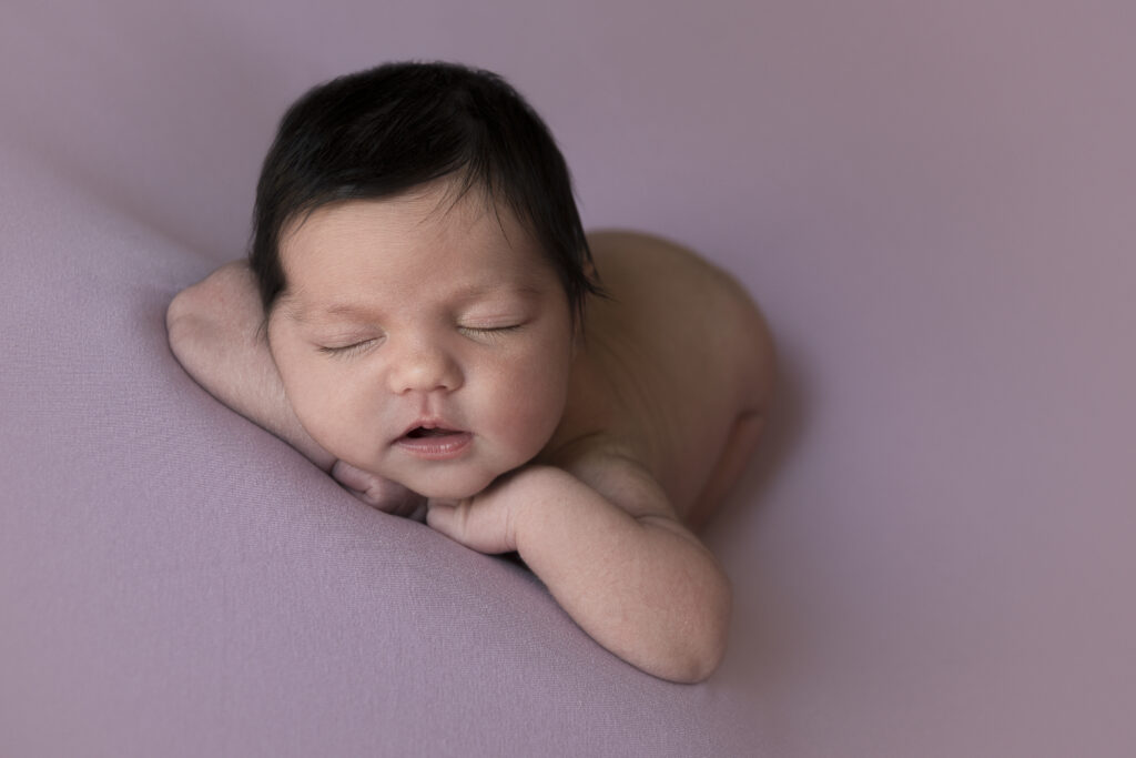 bebé recién nacido apoyado sobre sus brazos en pose newborn sobre fondo rosa