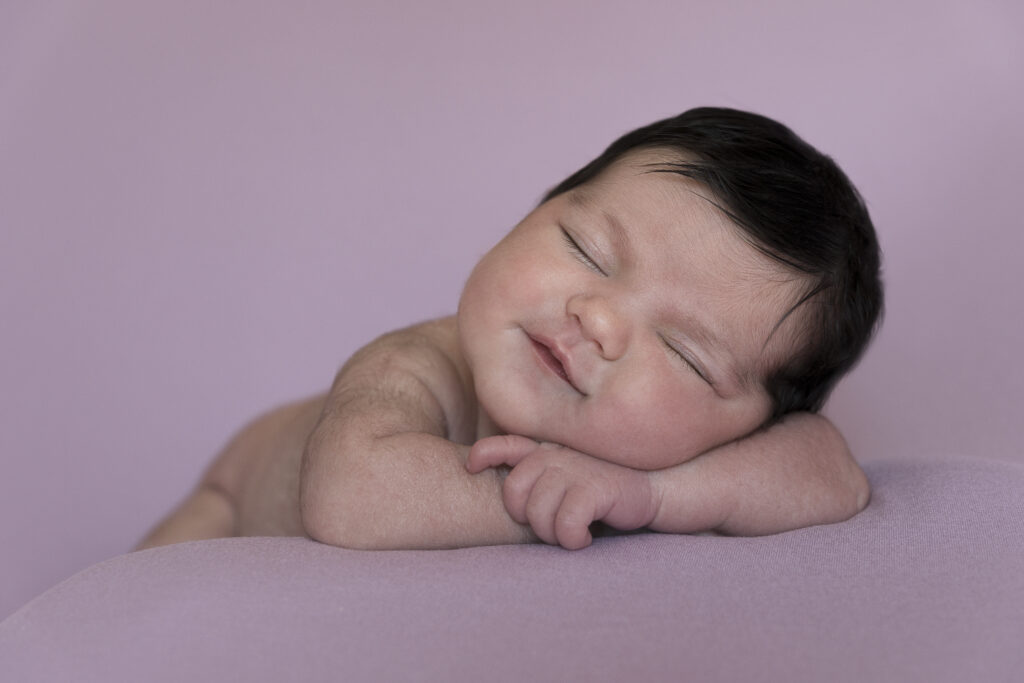bebé recién nacido sonriendo mientras duerme sobre fondo malva