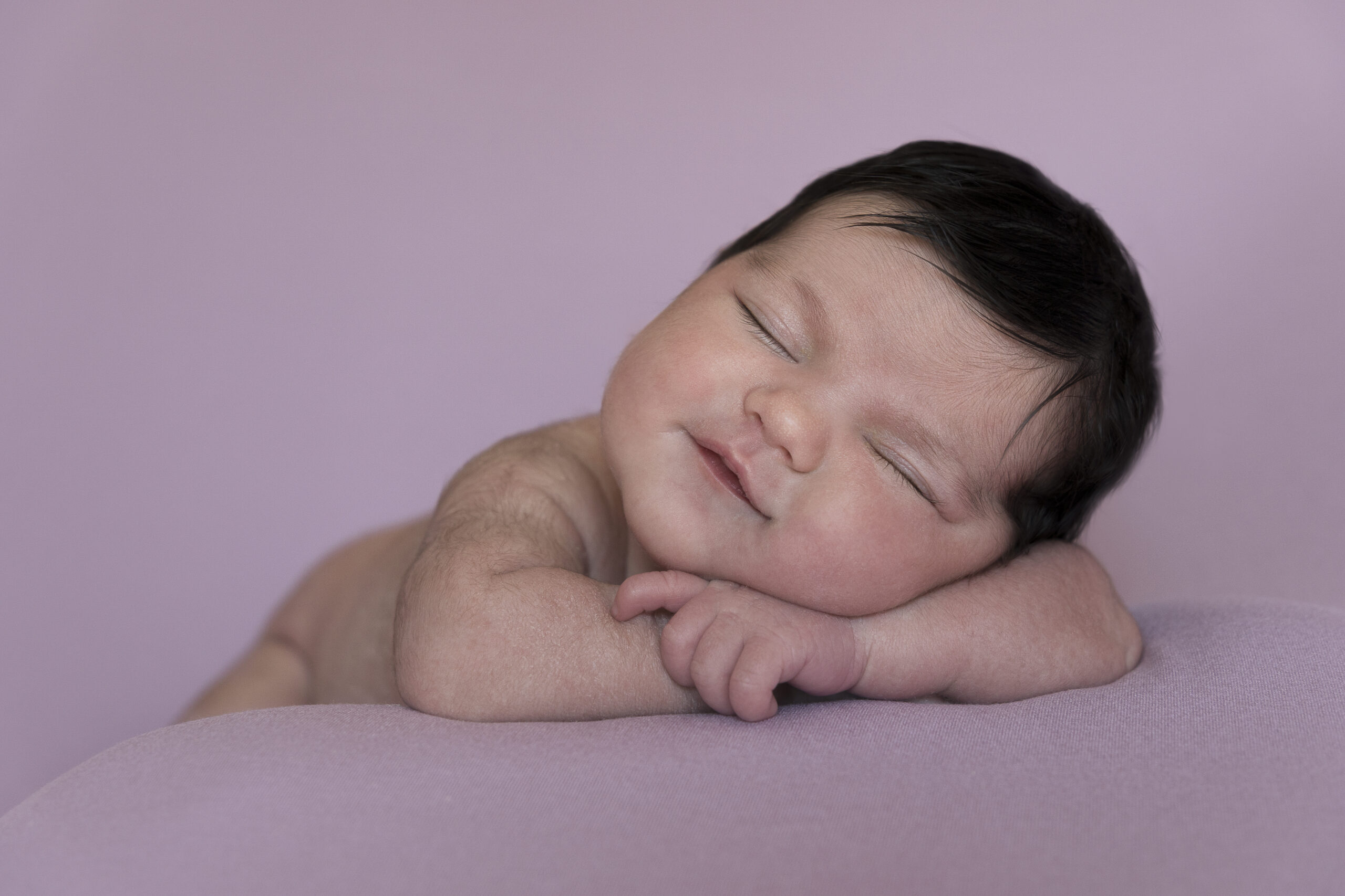 bebé recién nacido sonriendo mientras duerme sobre fondo malva