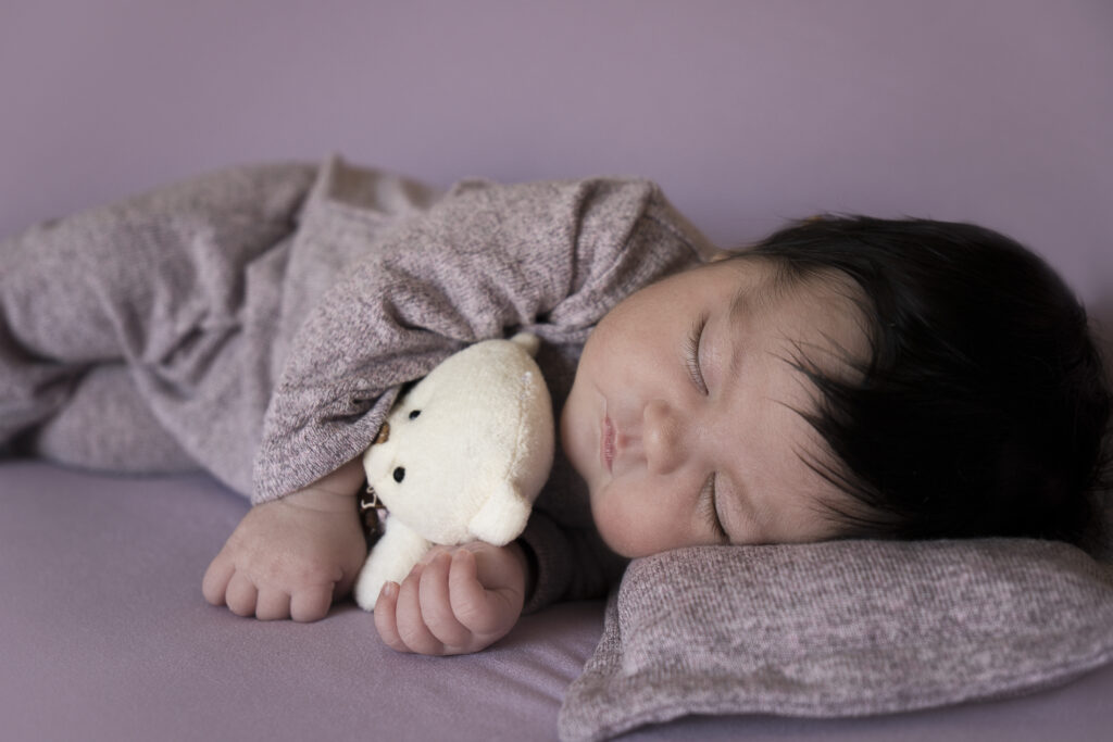 bebé recién nacido dormido abrazando un peluche sobre fondo malva bebé recién nacido dormido abrazando un peluche sobre fondo malva