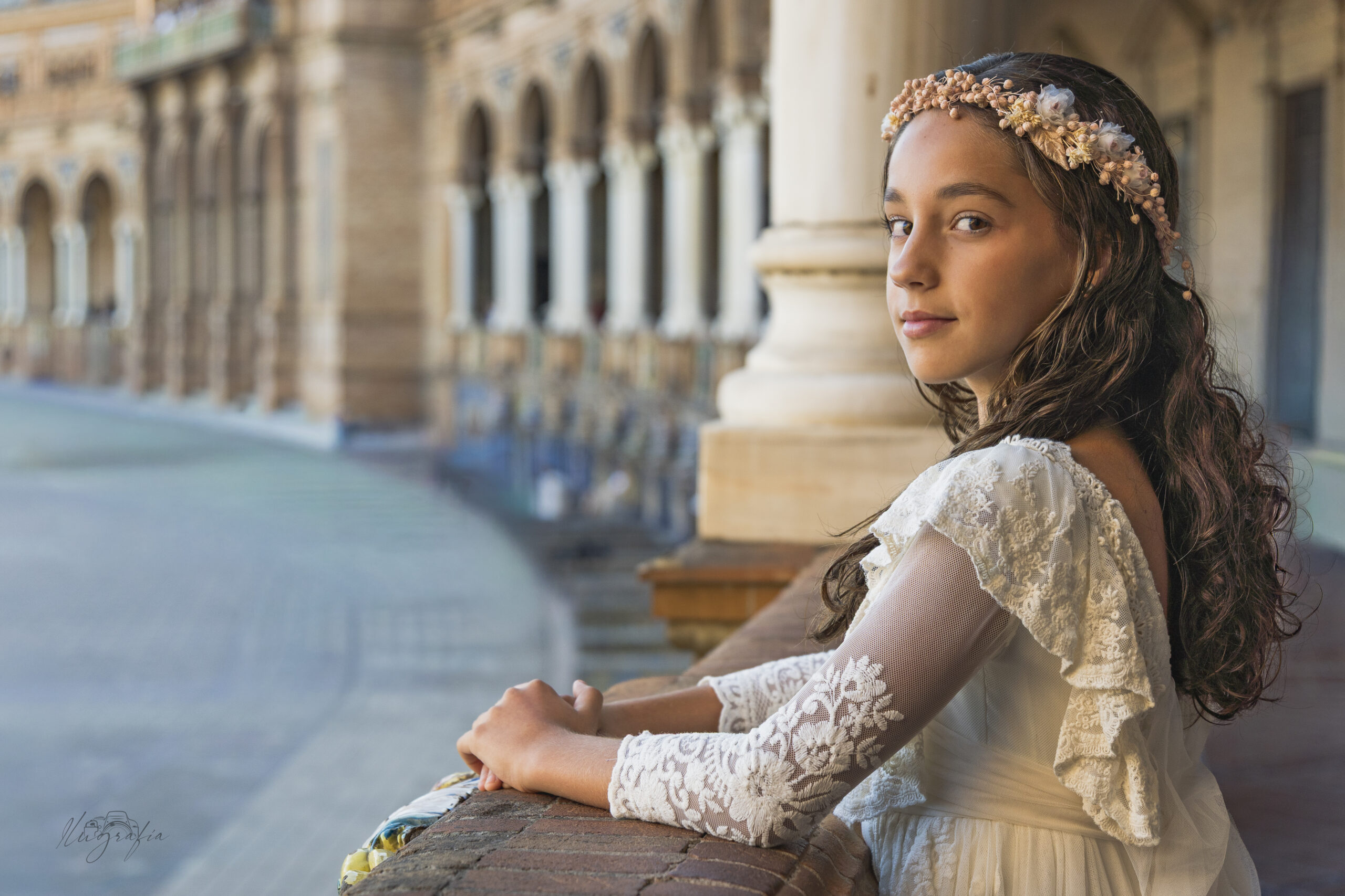 Niña de comunión apoyada en un muro con la Plaza de España desenfocada al fondo