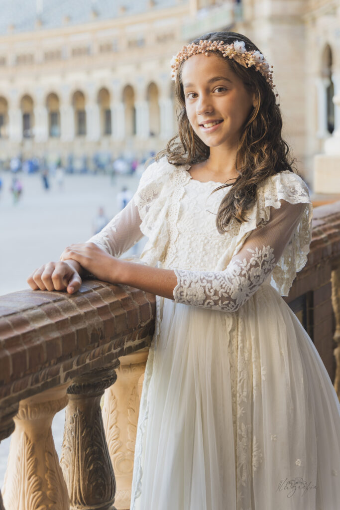 Niña de comunión apoyada en barandilla con vestido blanco