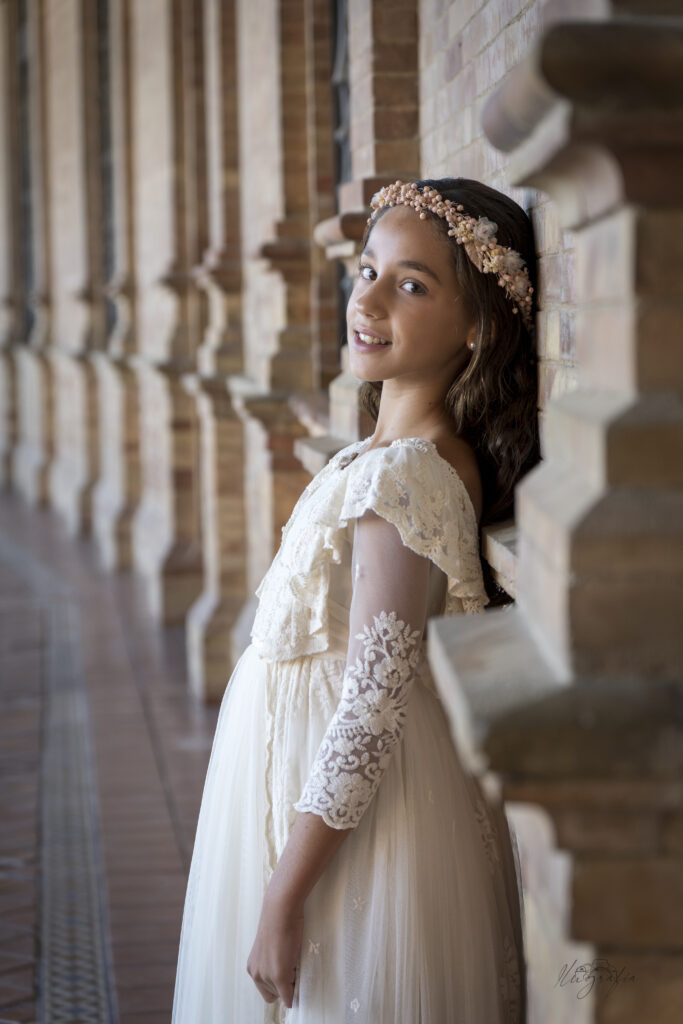 Niña de comunión apoyada en columna con vestido blanco
