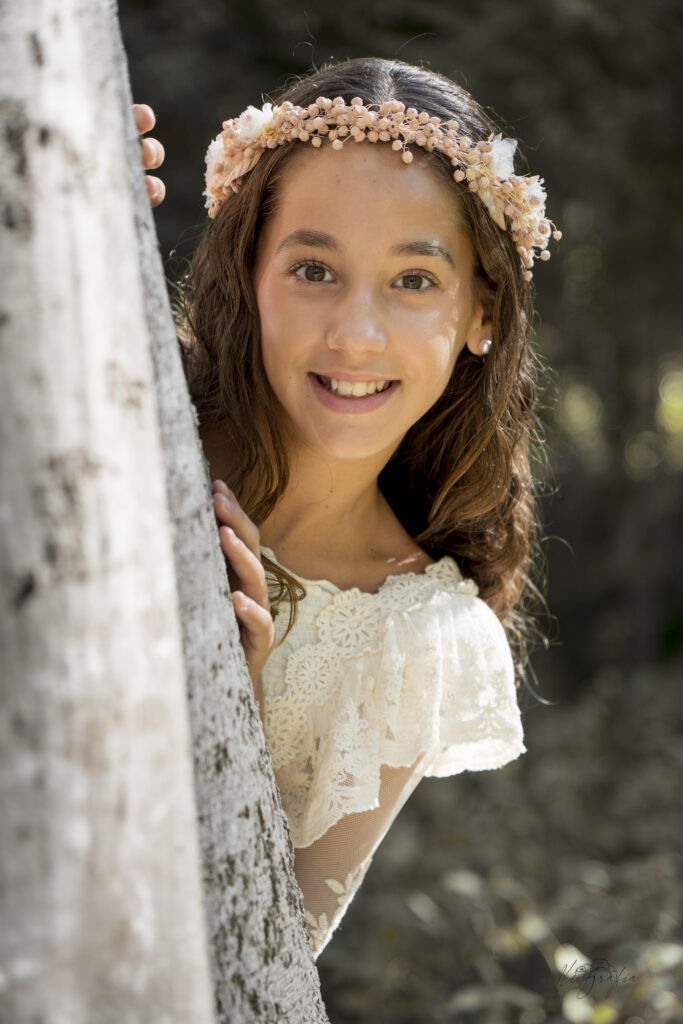 Niña de comunión asomada tras un árbol
